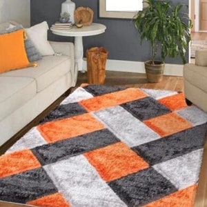 May include: A plush area rug with a geometric pattern in shades of orange, gray, and white. The rug has a soft, fluffy texture and is perfect for adding a touch of color and style to any room.