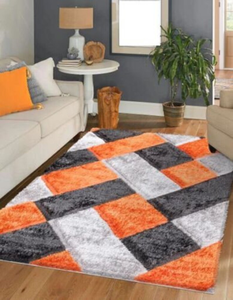 May include: A plush area rug with a geometric pattern in shades of orange, gray, and white. The rug has a soft, fluffy texture and is perfect for adding a touch of color and style to any room.