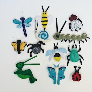May include: A collection of colorful felt insect ornaments, including a dragonfly, bee, butterfly, spider, beetle, and ladybug. The ornaments are in various colors, such as blue, yellow, black, green, and red. They are likely handmade and suitable for crafts or decoration.
