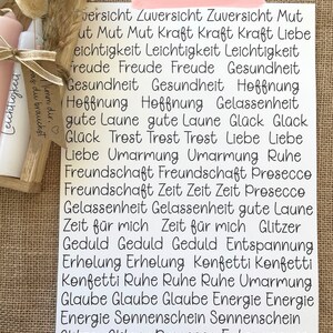 May include: A white card with black text listing positive words and phrases, including "Zuversicht", "Mut", "Kraft", "Liebe", "Freude", "Gesundheit", "Hoffnung", "Gl&uuml;ck", "Trost", "Umarmung", "Freundschaft", "Zeit", "Gelassenheit", "Geduld", "Erholung", "Konfetti", "Ruhe", "Glaube", "Energie", "Sonnenschein", "Glitzer", "Prosecco", "Entspannung", and "St&auml;rke".