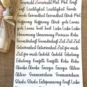 May include: A white sheet of paper with black text in a handwritten font. The text reads "Schrift 3" and lists a variety of words in German, including "Zuversicht", "Mut", "Kraft", "Leichtigkeit", "Freude", "Gesundheit", "Gl&uuml;ck", "Hoffnung", "Liebe", "Umarmung", "Freundschaft", "Zeit", "Gelassenheit", "Geduld", "Erholung", "Konfetti", "Ruhe", "Glaube", "Energie", "Glitzer", "Sonnenschein", "St&auml;rke", "Entspannung".