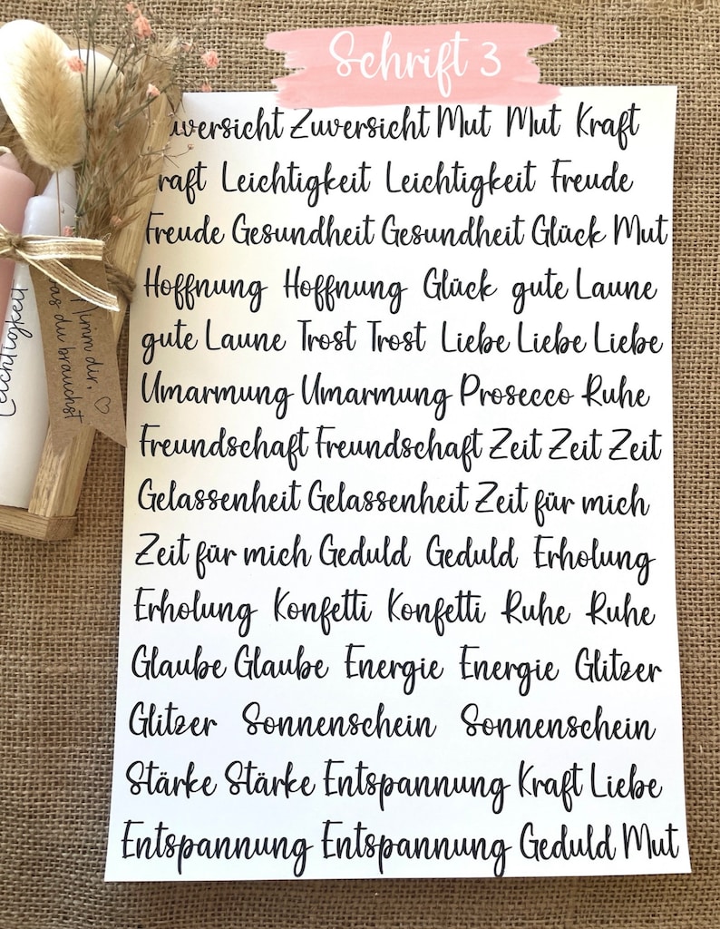 May include: A white sheet of paper with black text in a handwritten font. The text reads "Schrift 3" and lists a variety of words in German, including "Zuversicht", "Mut", "Kraft", "Leichtigkeit", "Freude", "Gesundheit", "Gl&uuml;ck", "Hoffnung", "Liebe", "Umarmung", "Freundschaft", "Zeit", "Gelassenheit", "Geduld", "Erholung", "Konfetti", "Ruhe", "Glaube", "Energie", "Glitzer", "Sonnenschein", "St&auml;rke", "Entspannung".