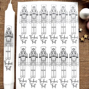 Könnte beinhalten: Ein Blatt mit druckbaren Aufklebern mit Schwarzweiß-Illustrationen von Nussknackerfiguren. Jeder Aufkleber hat den Text "Frohes Fest" unter dem Nussknacker.