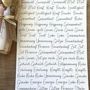 May include: A white card with black handwritten text. The text is in German and includes words like "Zuversicht", "Mut", "Kraft", "Freude", "Leichtigkeit", "Gesundheit", "Hoffnung", "Liebe", "Sonnenschein", "Umarmung", "Glitzer", "Freundschaft", "Prosecco", "Zeit", "Ruhe", "Geduld", "Entspannung", "Erholung", "Konfetti", "Glaube", "Energie", "St&auml;rke".