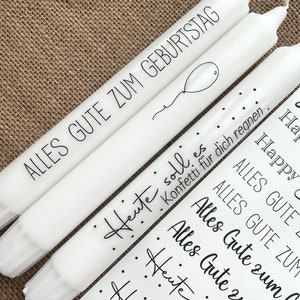 May include: Three white candles with black lettering. The candles have the text "Alles Gute zum Geburtstag" and "Heute soll es Konfetti f&uuml;r dich regnen."  The candles are decorated with black dots and a small balloon.