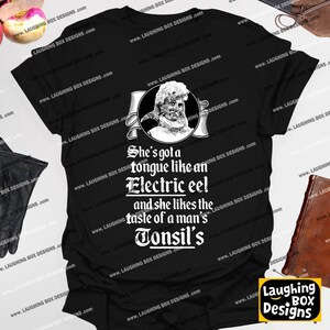 May include: Black t-shirt with the text "She's got a tongue like an Electric eel and she likes the taste of a man's Tonsil's." The shirt features a graphic of a person with a banner.