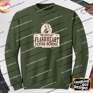 Può includere: Una felpa girocollo color verde oliva con una stampa grafica di una persona con i baffi sopra la scritta LORD FLASHHEART FLYING SCHOOL EST. 1917. Il design è centrato sul petto e utilizza caratteri di colore marrone scuro.