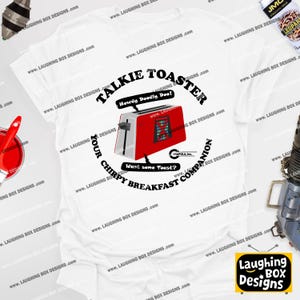 Puede incluir: Camiseta blanca con un diseño de tostadora roja y plateada. El diseño incluye el texto "Talkie Toaster", "Your Chirpy Breakfast Companion", "Howdy Doodly Doo!" y "Want some Toast?"