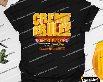 May include: Black t-shirt with a yellow and orange graphic that reads "CREME BRULEE" above text that says "IT'S A SHIT BUSINESS" and "Voodoo Lady". The shirt also says "Eurovision 1981".