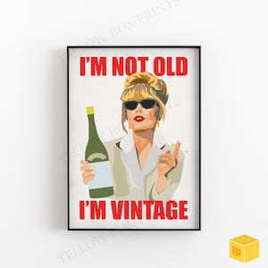 May include: A black framed print with a white background and red text that reads "I'm not old I'm vintage". A woman with blonde hair and sunglasses is holding a bottle of wine.