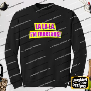 May include: A black long-sleeve crewneck sweatshirt featuring the text LA LA LA, I'M FABULOUS! printed in bright pink letters on two yellow rectangular backgrounds. The design is centered on the chest of the garment.