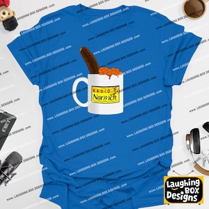 May include: A blue t-shirt features a graphic of a white mug filled with baked beans and a sausage. The mug has the text "Radio Norwich" on it. The shirt is from Laughing Box Designs.