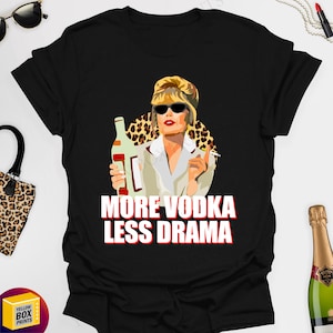 May include: A black t-shirt featuring a cartoon image of a woman holding a bottle of vodka. The text "More Vodka Less Drama" is printed in white on the shirt.