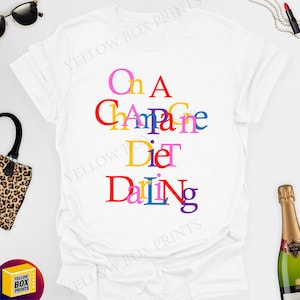 May include: White t-shirt with the text "On A Champagne Diet Darling" in colourful letters.
