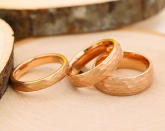 May include: Three gold-toned wedding bands with a hammered texture. The bands are stacked on top of each other on a wooden surface.