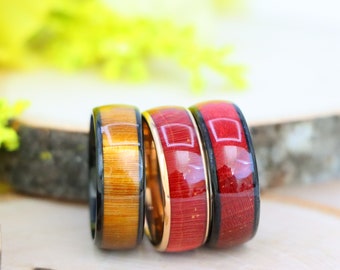 May include: Three wooden rings with black and gold metal bands. The rings are in different colors: brown, red, and dark red.