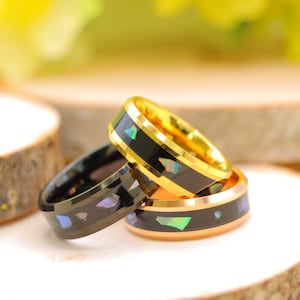 May include: Three men's wedding bands with black and gold inlay. The bands are stacked on top of each other. The top band is gold with black inlay. The middle band is black with gold inlay. The bottom band is black with iridescent inlay.