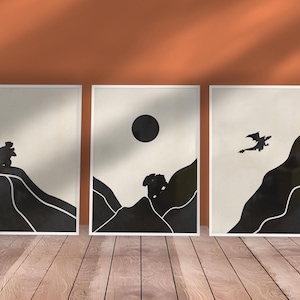 Könnte beinhalten: Drei gerahmte Kunstdrucke mit minimalistischen schwarz-weißen Berg- und Drachensilhouetten. Das Kunstwerk zeigt eine Sonne und einen Drachen und schafft eine ruhige Landschaft. Die Drucke werden auf einem Holzboden ausgestellt.