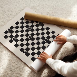 May include: A black and white chess board print with chess piece silhouettes. A rolled-up print and a cardboard tube are next to the board. The board is on a light-colored carpet.