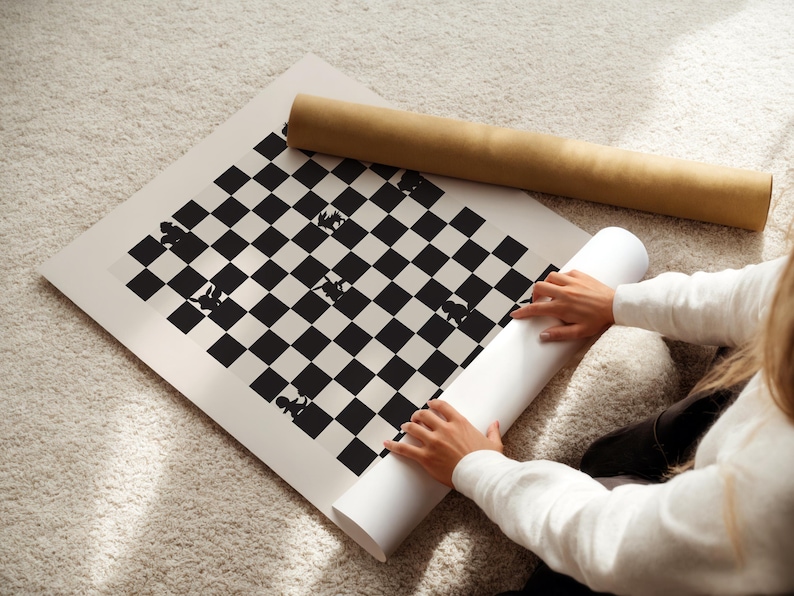 May include: A black and white chess board print with chess piece silhouettes. A rolled-up print and a cardboard tube are next to the board. The board is on a light-colored carpet.