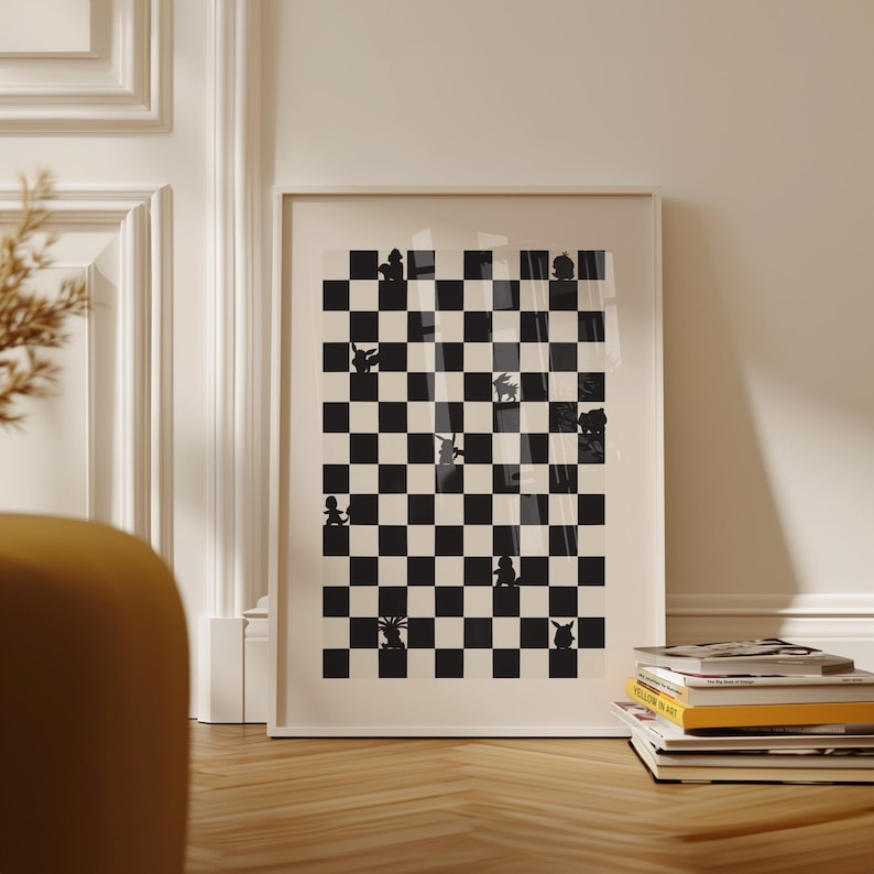May include: Framed art print featuring a black and white checkerboard design with various silhouette figures. The artwork is displayed on a wooden floor, leaning against a white wall. A stack of books is visible in the foreground.