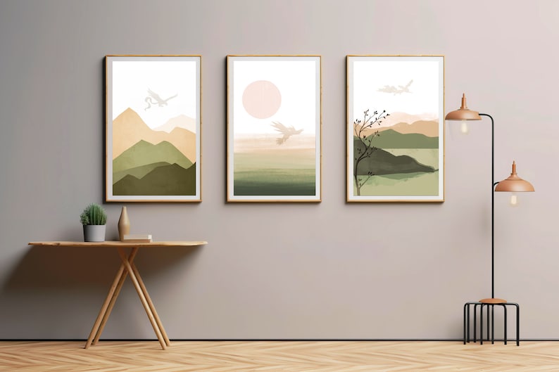 May include: Three framed abstract landscape prints with a muted color palette of green, brown, and beige. The prints feature stylized mountains, a sun, and a tree with birds flying overhead.