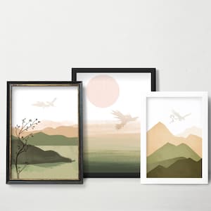 May include: Three framed abstract landscape prints with a minimalist style. The prints feature a muted color palette of green, brown, and beige. Each print depicts a mountain range with a bird flying overhead. The frames are black, gold, and white.