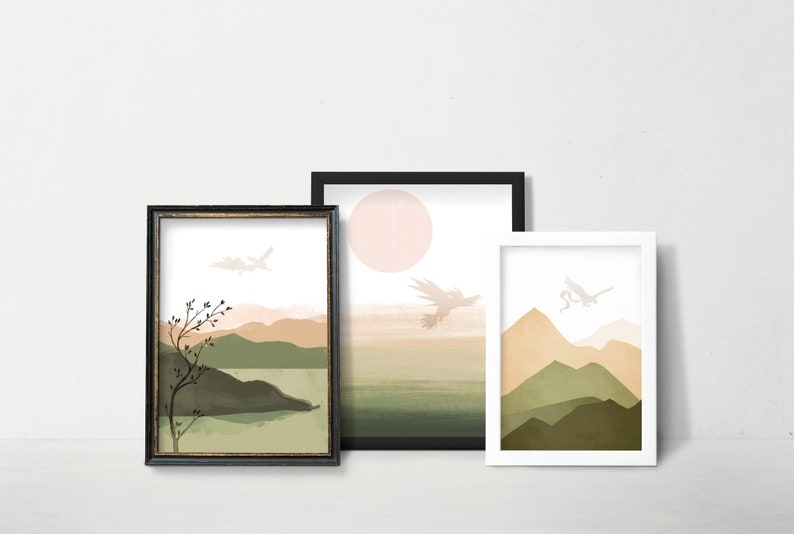 May include: Three framed abstract landscape prints with a minimalist style. The prints feature a muted color palette of green, brown, and beige. Each print depicts a mountain range with a bird flying overhead. The frames are black, gold, and white.