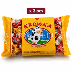 May include: A clear plastic bag containing three packs of Krówka milk cream fudge sweets. The yellow label features a cartoon cow, the text Krówka, Morus Deluxe, and Milk Cream Fudge, with a net weight of 1 kg printed on the front.