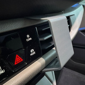 Könnte beinhalten: Eine graue Handyhalterung für die Lüftungsschlitze eines Autos, die im Armaturenbrett eines Fahrzeugs installiert ist. Die Halterung ist für die Aufnahme eines Telefons konzipiert und befindet sich in der Nähe der Lüftungsschlitze. Das Armaturenbrett hat Knöpfe mit der Aufschrift "CLIMA" und "MODE".