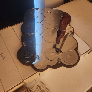 Puede incluir: Una escultura de metal plateado en forma de nube hecha de círculos superpuestos. La escultura está sobre una base de madera marrón. La escultura está rodeada de cajas con la palabra "Cards" impresa en ellas.