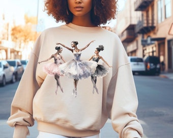 May include: A beige sweatshirt with a graphic print of three ballerinas in various poses. The ballerinas are wearing tutus in shades of pink, gray, and black.