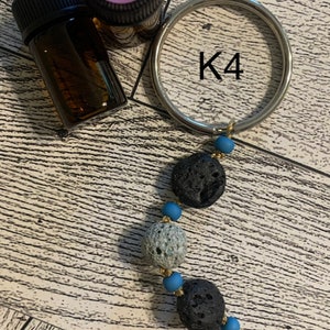May include: A silver key ring with the letter K4 printed on it. A string of blue beads and black lava rock beads hangs from the key ring.