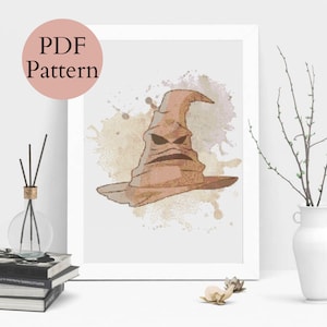 May include: A brown and black Sorting Hat with a grumpy face, surrounded by watercolor-style splatters on a white background.
