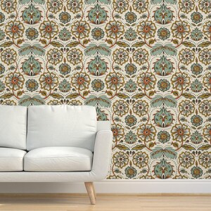 May include: A cream-colored floral wallpaper with a repeating pattern of stylized flowers and leaves in shades of orange, teal, and gold. The wallpaper is installed on a wall next to a white sofa.