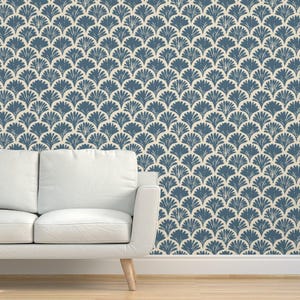 May include: A white couch sits in front of a wall covered in blue and white patterned wallpaper. The wallpaper features a repeating pattern of stylized fan shapes.