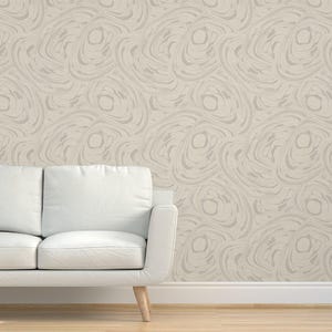 May include: A white couch sits in front of a wall covered in a beige wallpaper with a swirling pattern.