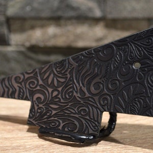 Puede incluir: Golpeador de guitarra negro con un patrón floral en relieve decorativo.