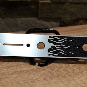 May include: A silver guitar control plate with a black flame design. The plate has four holes for mounting screws and a single hole for a knob.