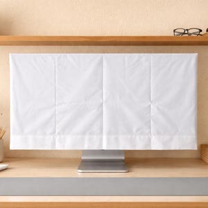 May include: A white computer monitor cover made of fabric, covering the screen of a silver computer monitor. The cover is rectangular and has vertical seams. The monitor sits on a wooden desk.