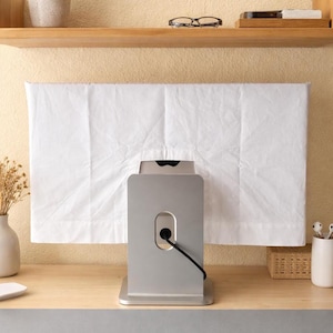 May include: A silver computer monitor stand with a black power cord. A white sheet is draped over the monitor. The stand is on a wooden desk with a gray mousepad. A small plant and other desk accessories are on a shelf above.