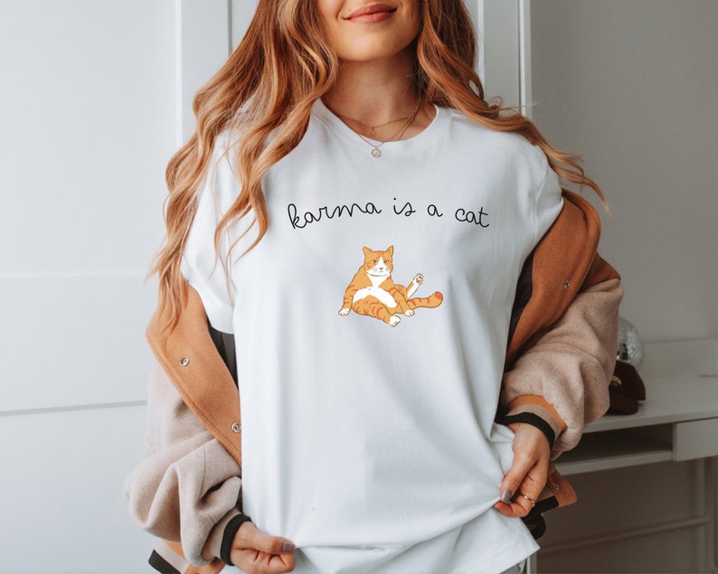 May include: White t-shirt with the text "karma is a cat" and a cartoon orange cat illustration.