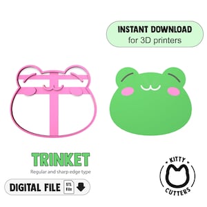 Puede incluir: Un contorno rosa en forma de rana y un diseño verde en forma de rana. El texto incluye "DESCARGA INSTANTÁNEA para impresoras 3D", "TRINKET", "ARCHIVO DIGITAL" y "KITTY CUTTERS".