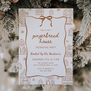 May include: A white invitation card with a brown gingerbread house design, bow, and text. The card is for a gingerbread house decorating party hosted by the Hudson's on November 27th at 5 PM. The card is surrounded by a Christmas tree.