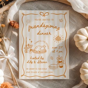 May include: A Friendsgiving dinner invitation card with a decorative border, featuring text and illustrations in brown. The card is surrounded by white pumpkins, dried flowers, and a bamboo ring. The invitation is hosted by Lily & Steven.