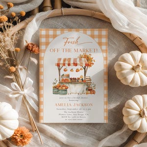 Op de afbeelding: Een uitnodiging voor een bruidsdouche met een markt thema. De uitnodiging bevat een aquarel illustratie van een marktkraam met pompoenen en producten. De tekst luidt "Fresh Off The Market!" en bevat evenement details.