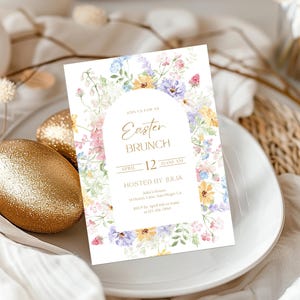 Op de afbeelding: Een uitnodigingskaart voor een Paasbrunch met een bloemen aquarelontwerp. De kaart toont de tekst "Easter Brunch" en details voor het evenement, inclusief datum en tijd. De uitnodiging is omgeven door kleurrijke bloemen en ligt op een wit bord.