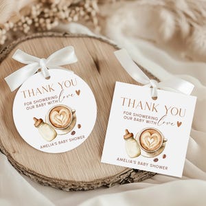 May include: Two baby shower thank you tags with white ribbon. One is round, the other square. Both have the text "THANK YOU FOR SHOWERING OUR BABY WITH love" and a coffee cup design with a heart in the foam.