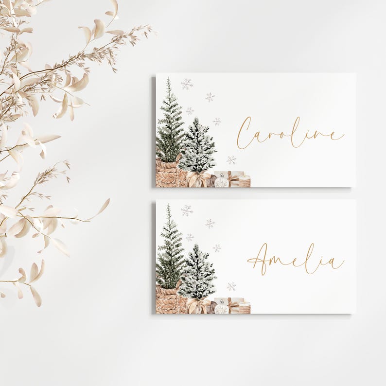 Puede incluir: Dos tarjetas rectangulares blancas con texto dorado e ilustraciones de acuarela. Cada tarjeta presenta un &aacute;rbol de Navidad en una cesta tejida, regalos y copos de nieve. Una tarjeta dice "Caroline" y la otra "Amelia".