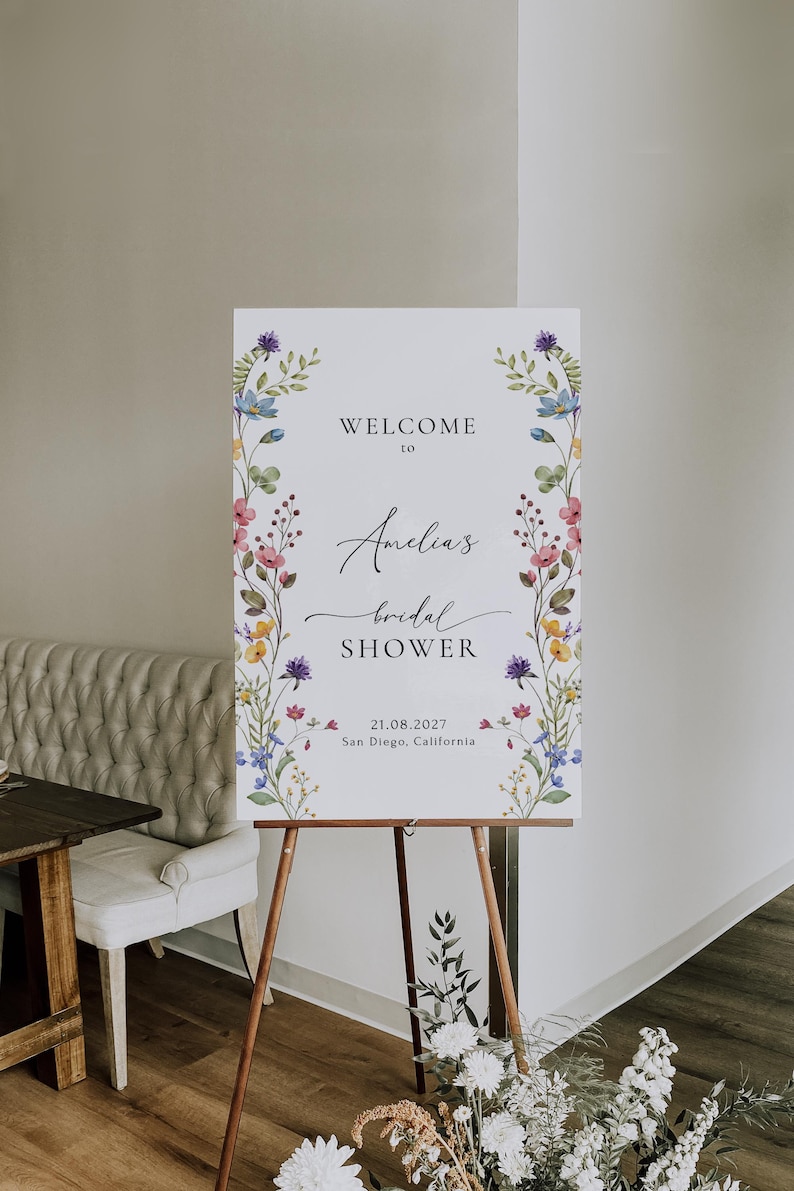 May include: A white welcome sign with a floral border and the text "Welcome to Amelia's bridal shower 21.08.2027 San Diego, California".